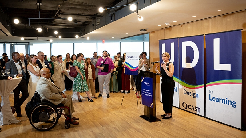 Photo of 飞艇168开奖体彩结果网 CEO Lindsay Jones speaking to event guests, standing in front of three banners spelling out UDL.